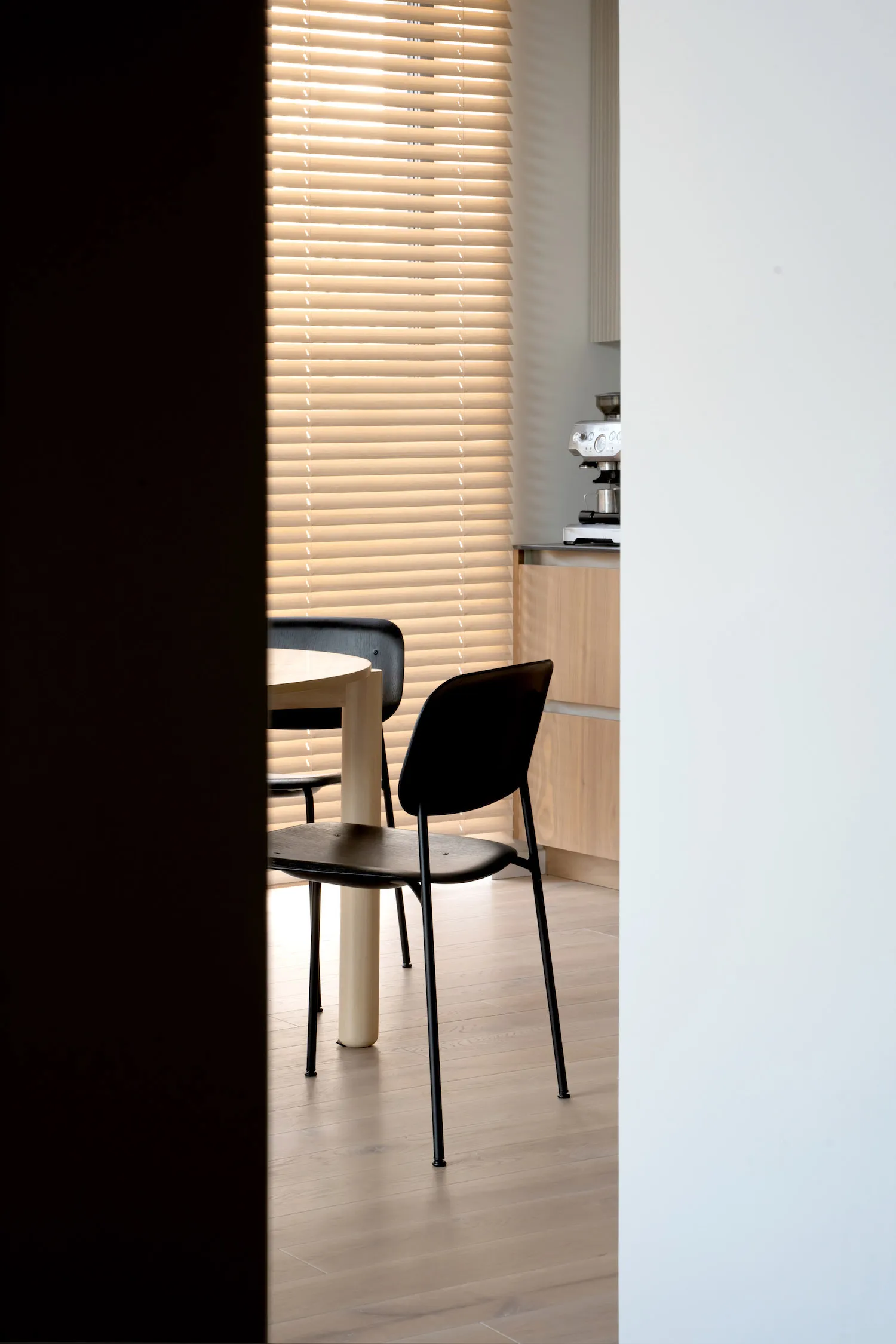 Minimalist kitchen with black chairs and wooden table, blinds closed.