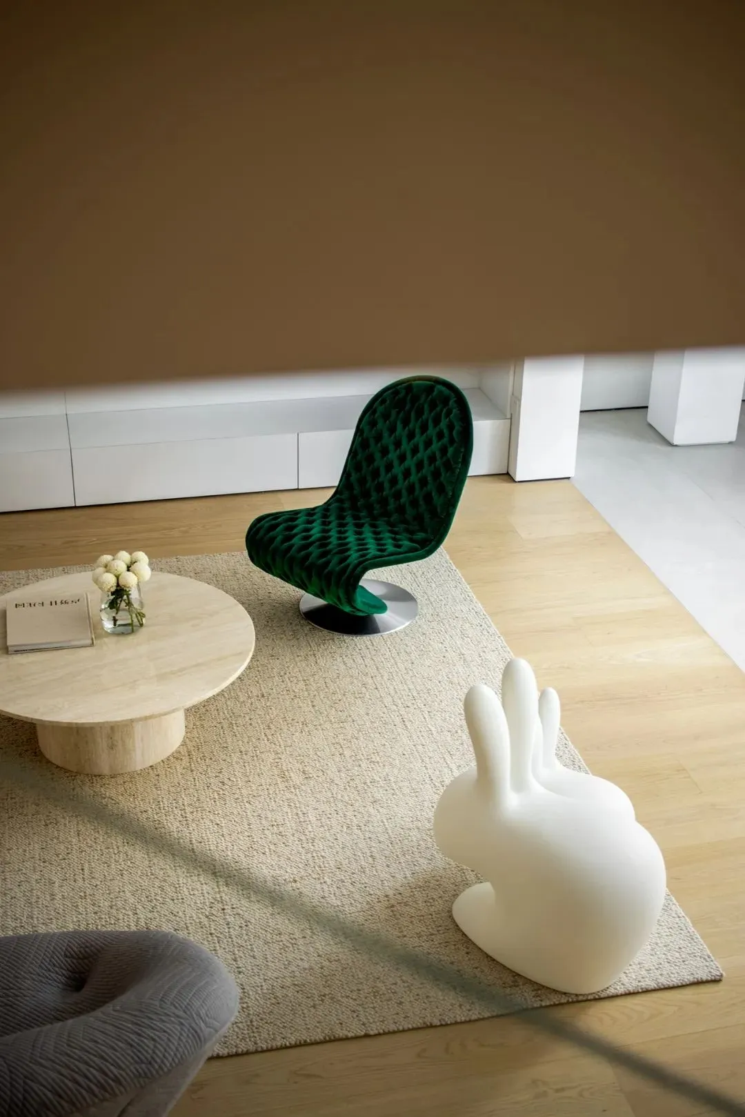 A modern living room featuring a green upholstered chair, a white sculpture, and a wooden coffee table.