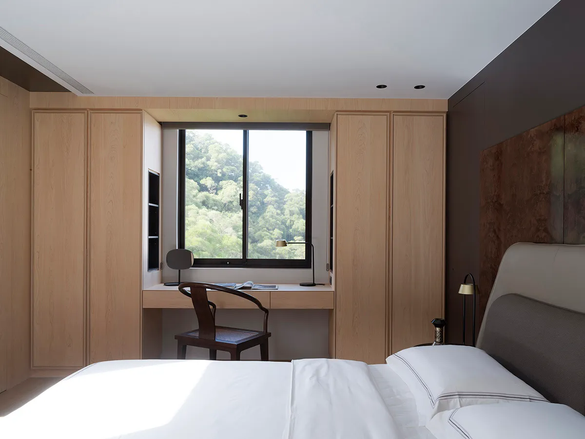 Modern minimalist bedroom with white wood-paneled walls and cabinets, featuring a white bed with pillows, a desk area by the