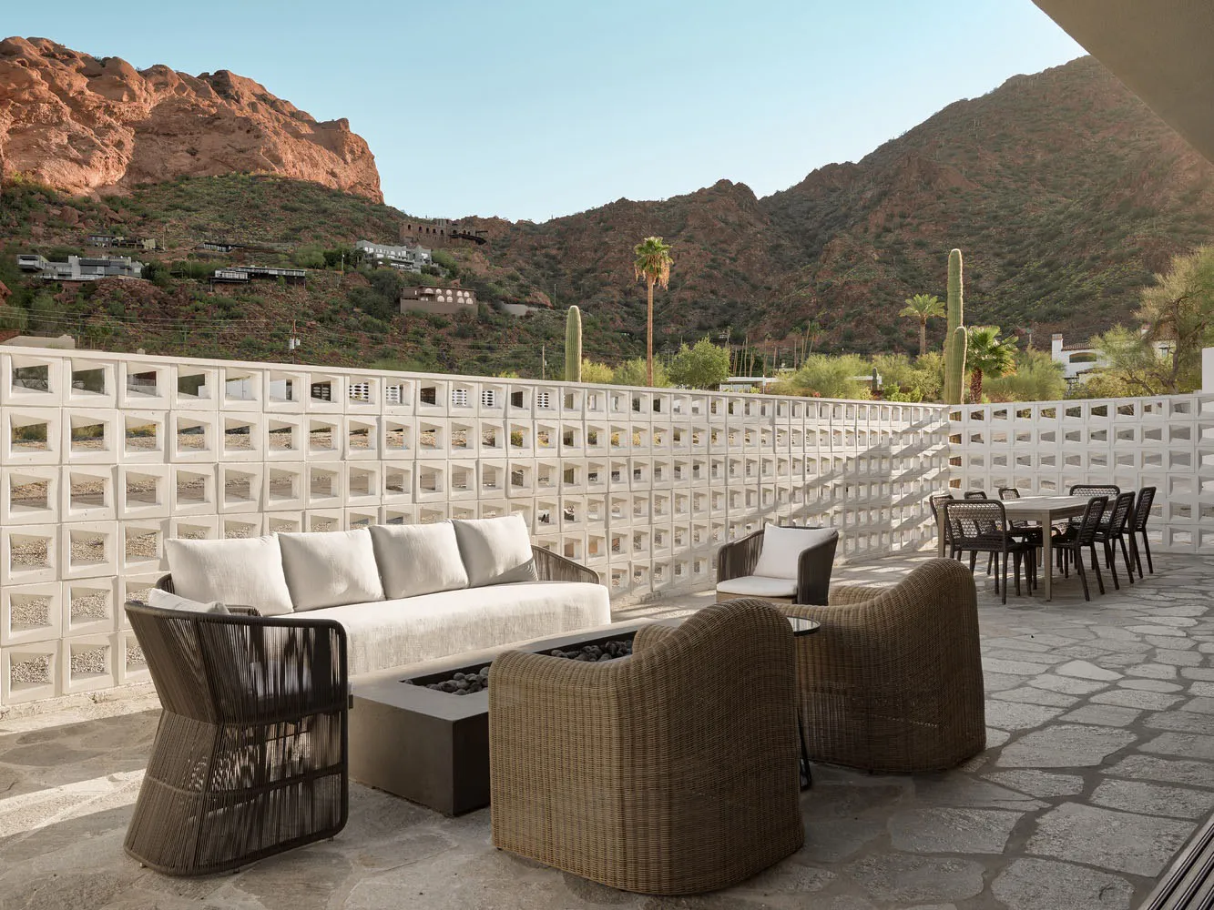 Modern outdoor living area with concrete and wicker furniture, surrounded by mountains.