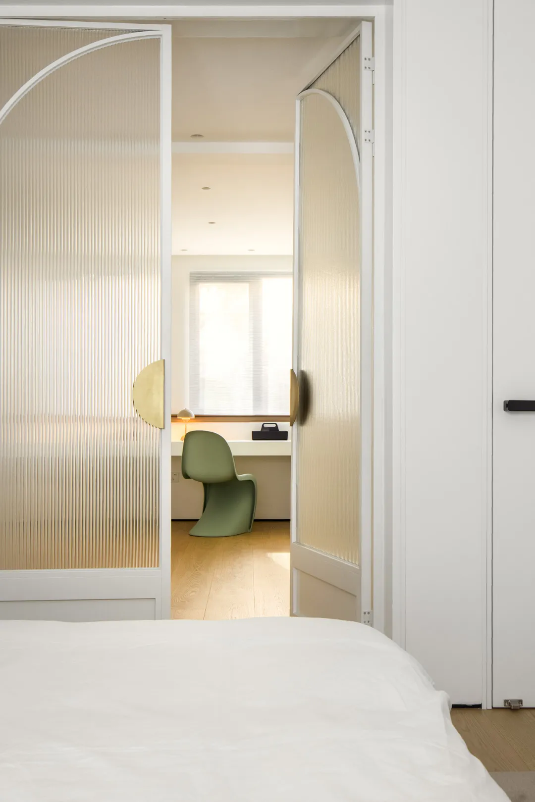 A minimalist bedroom with glass doors and a green chair.