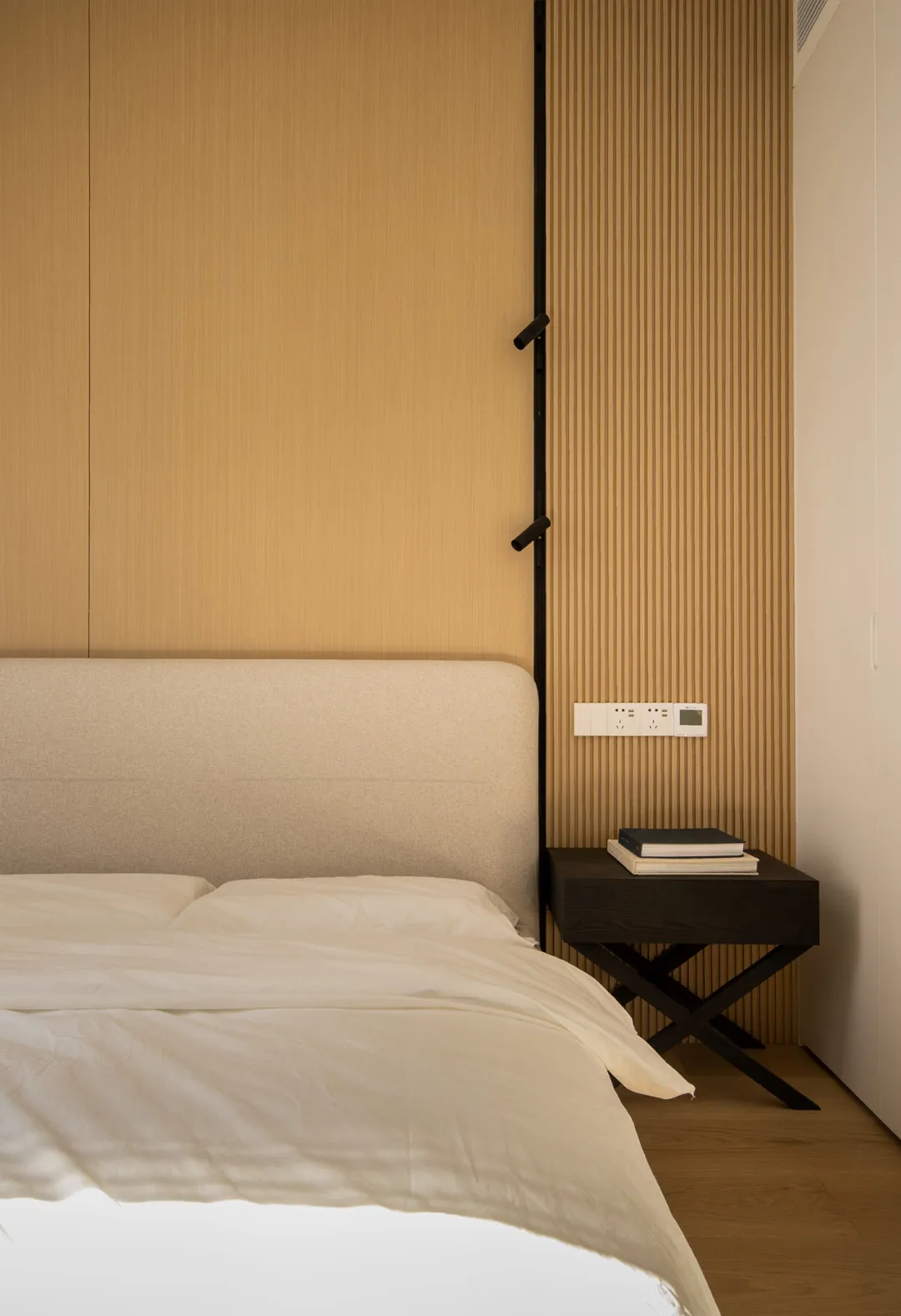 A minimalist bedroom featuring a bed with a fabric headboard and a nightstand with books and reading materials.