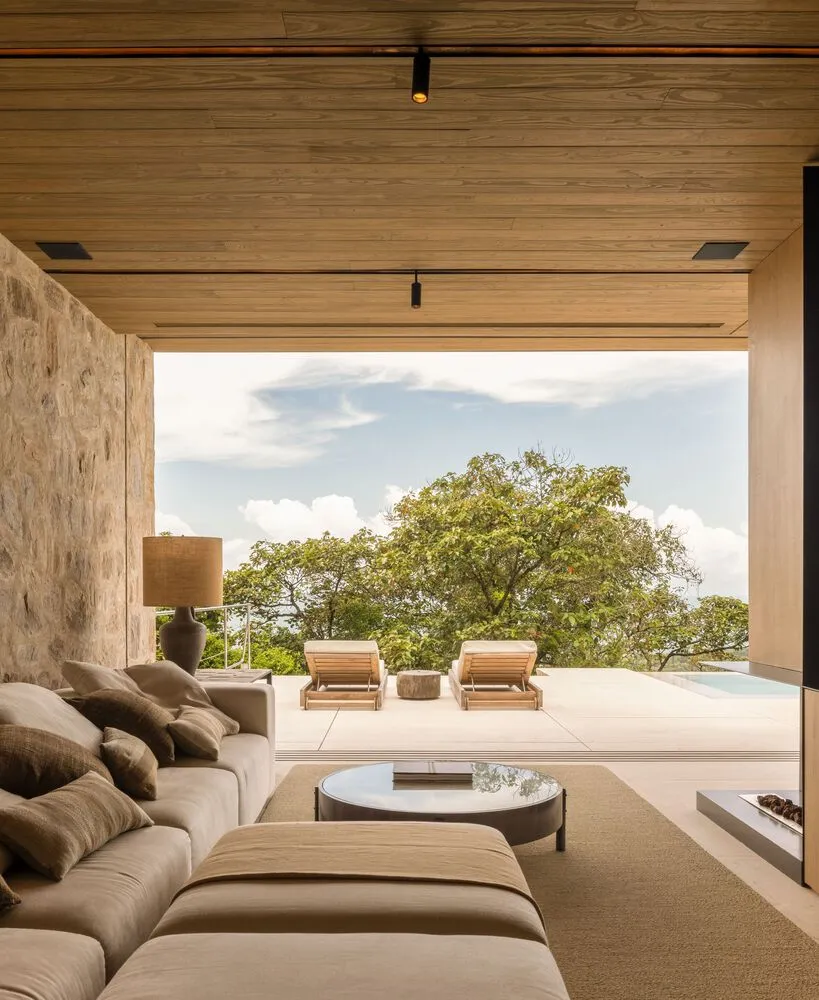A minimalist living room featuring wood and stone materials with a comfortable seating area and a view of the outdoors.