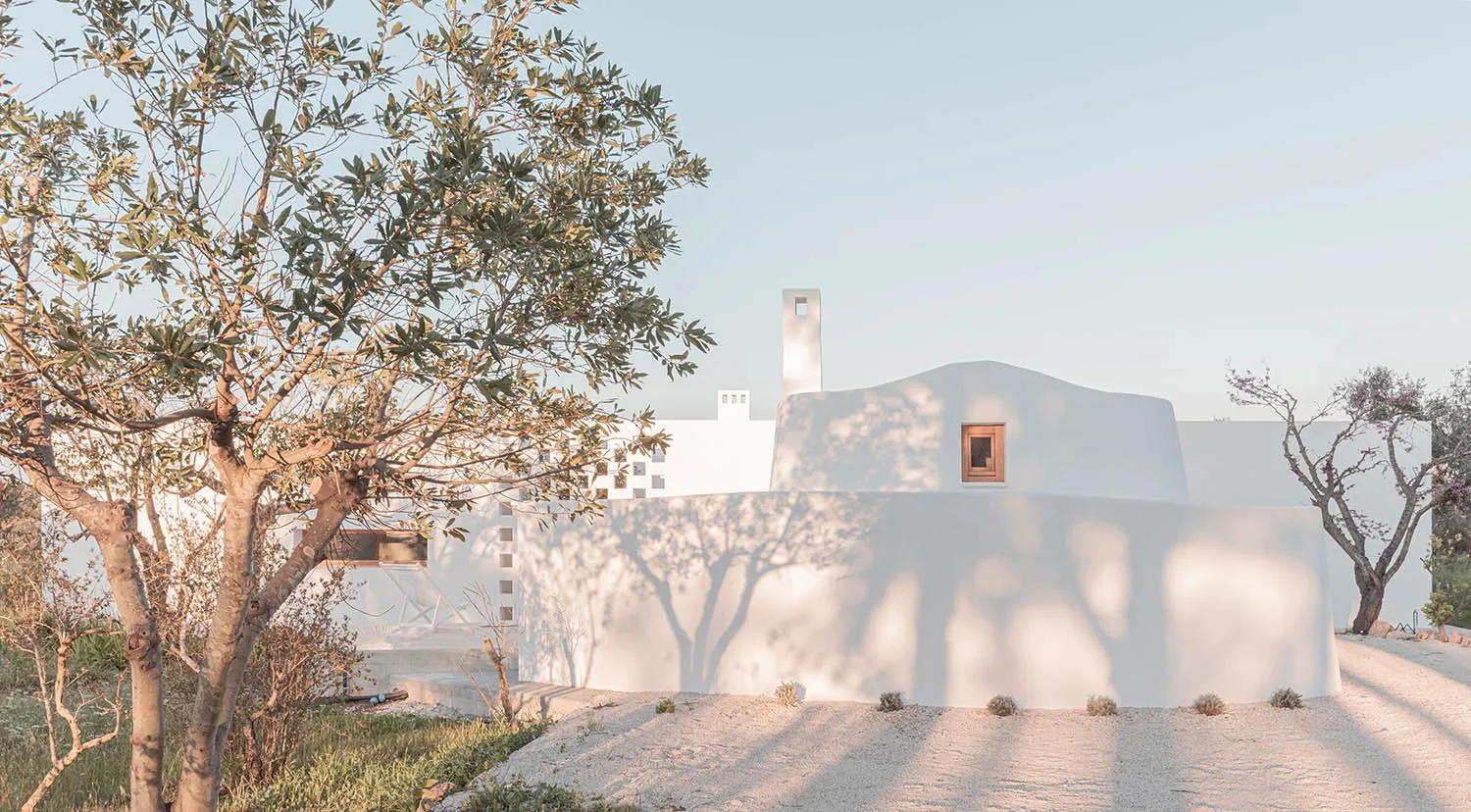 Minimalist white plaster exterior home with tree shadows cast on the wall.