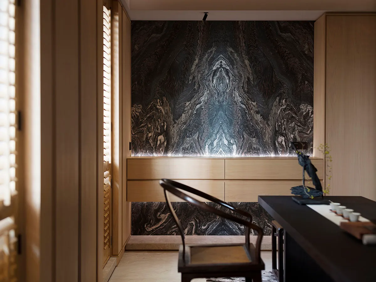 Modern living room featuring marble walls and wooden furniture with a black table and chair.