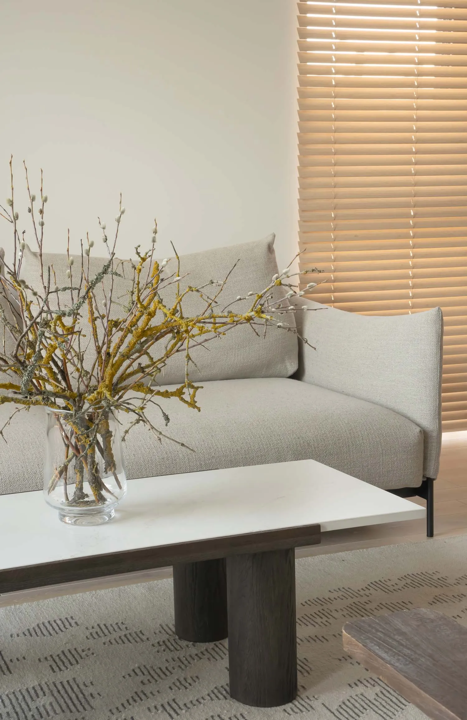 Modern, minimalist living room with a white coffee table, beige sofa, and gray and wood accent table.