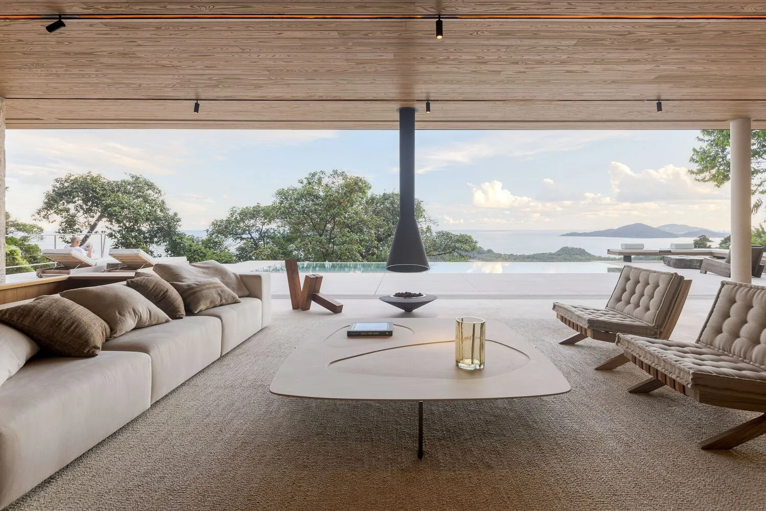 Contemporary minimalist living room with white leather sofas and a glass fireplace on a wooden patio overlooking the ocean.