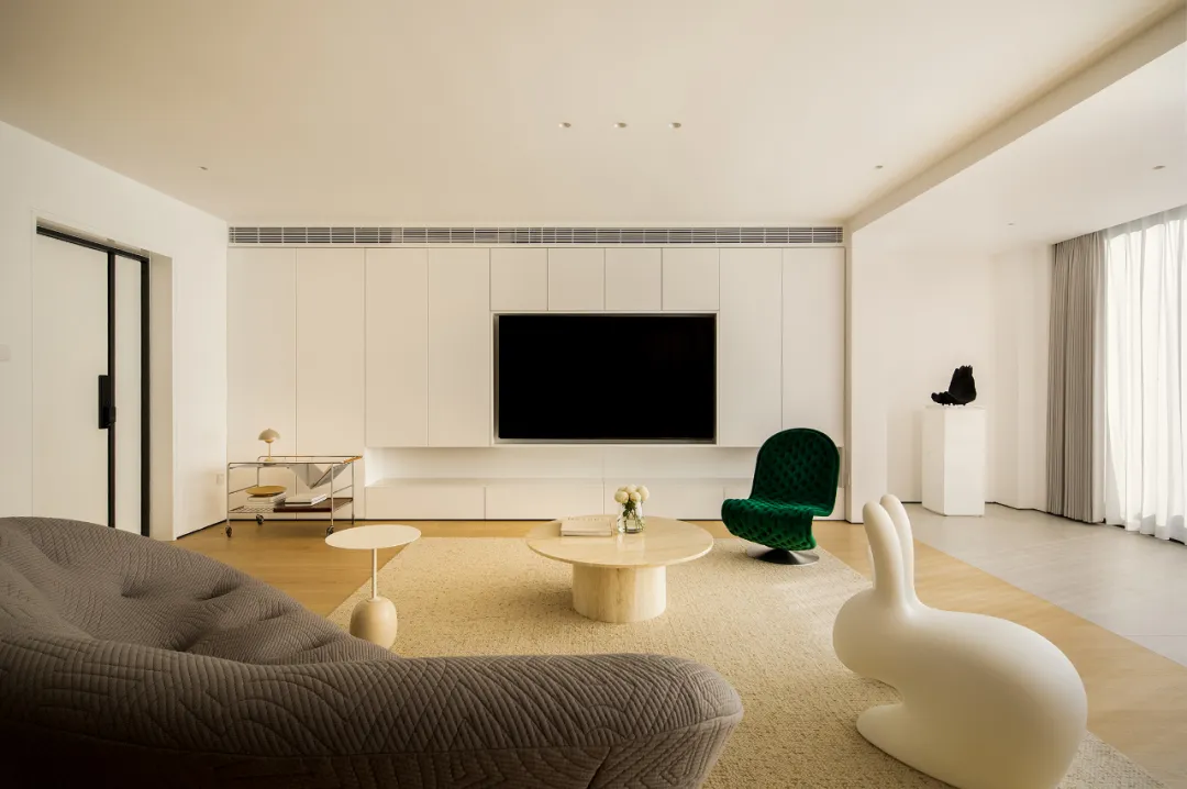 Modern minimalist living room with white furniture and a large television in the background.