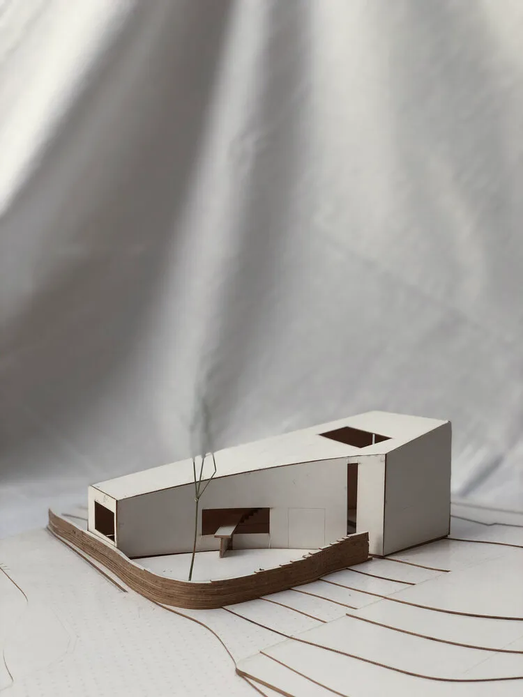 以紙板材料製作的現代住宅建築模型，置於白色表面，呈現平面圖配置線條。