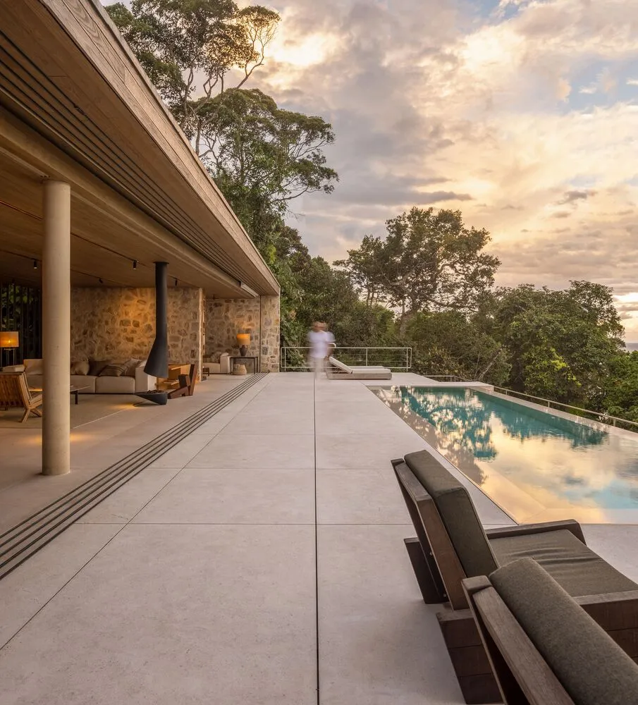A modern residential outdoor patio featuring concrete, wood, stone, and glass elements.