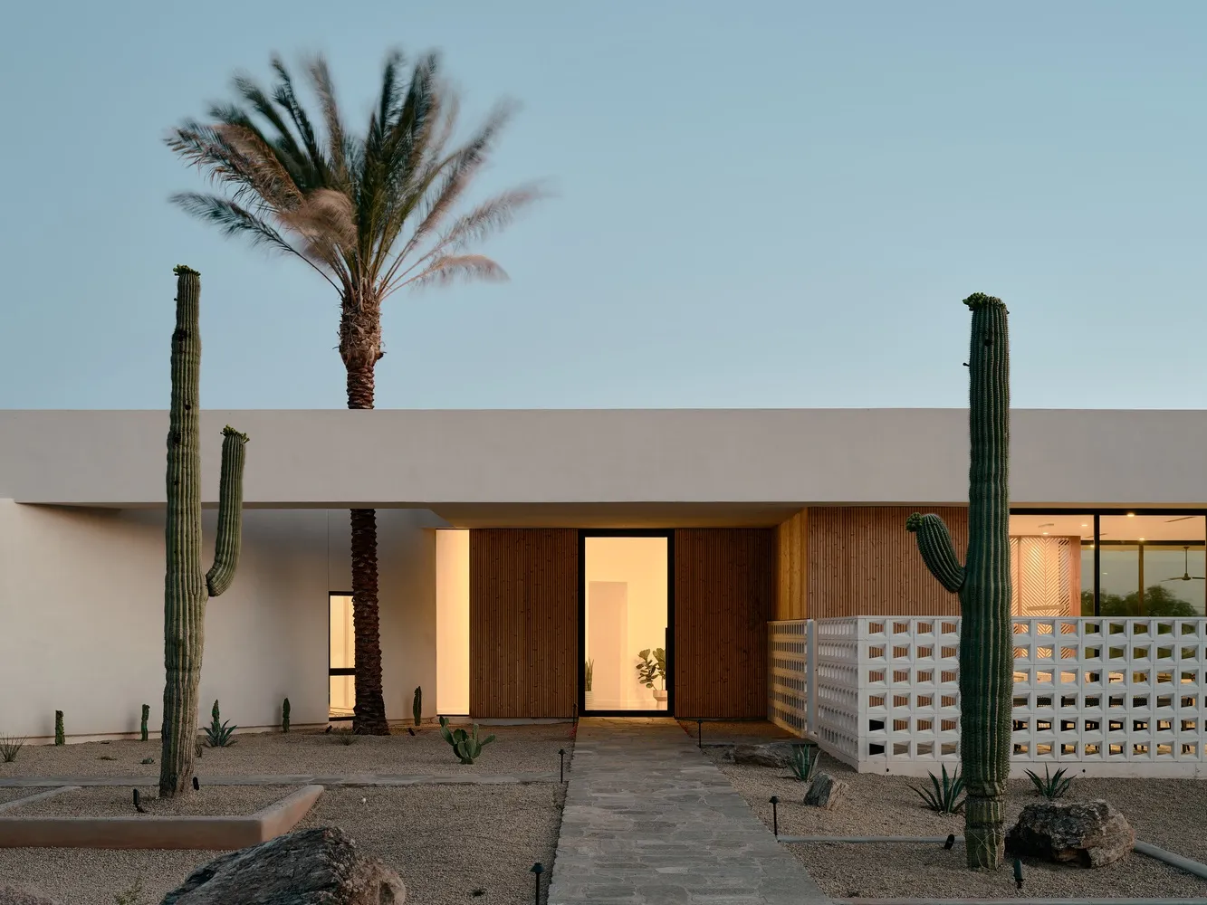 A modern house with stucco exterior, large windows, and a palm tree in the background.