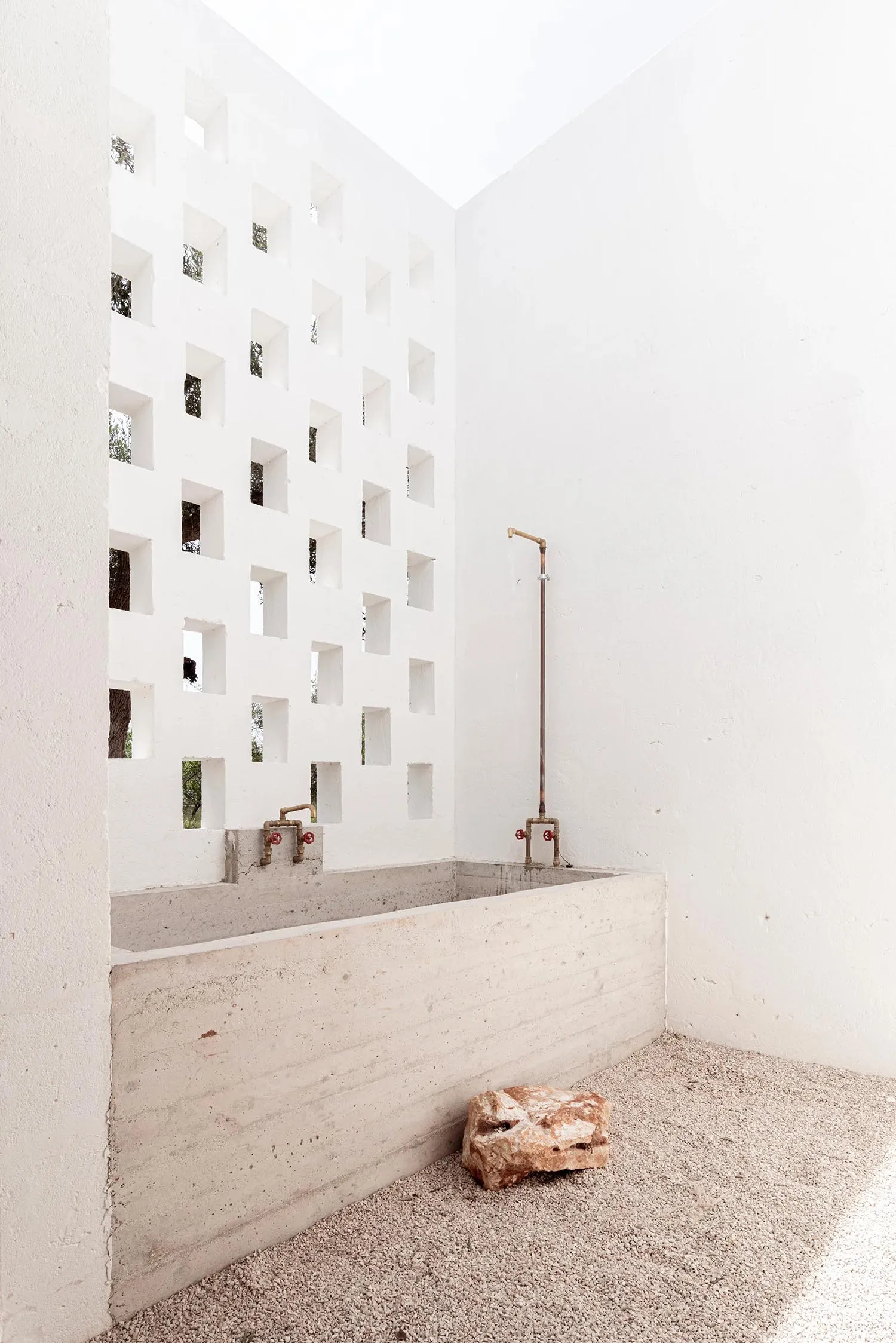 A minimalist industrial-style bathroom with concrete walls and floors, featuring a walk-in shower and a rock-like object on t