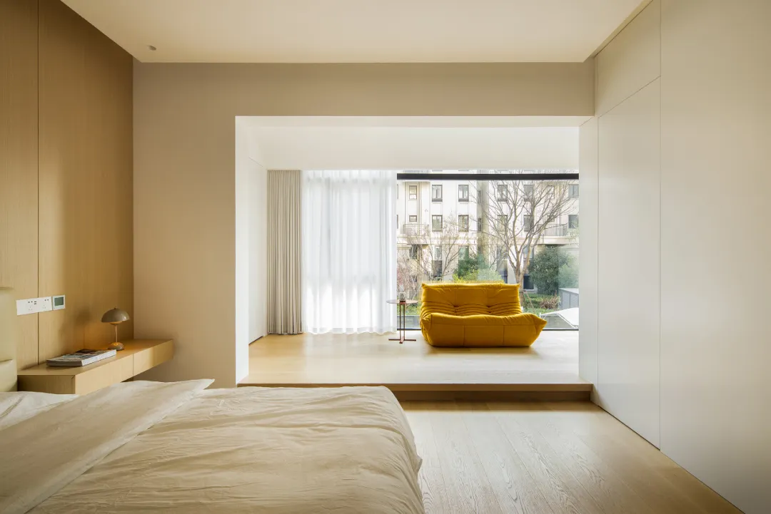 Modern minimalist bedroom with a yellow sofa, light wood flooring, and white walls.