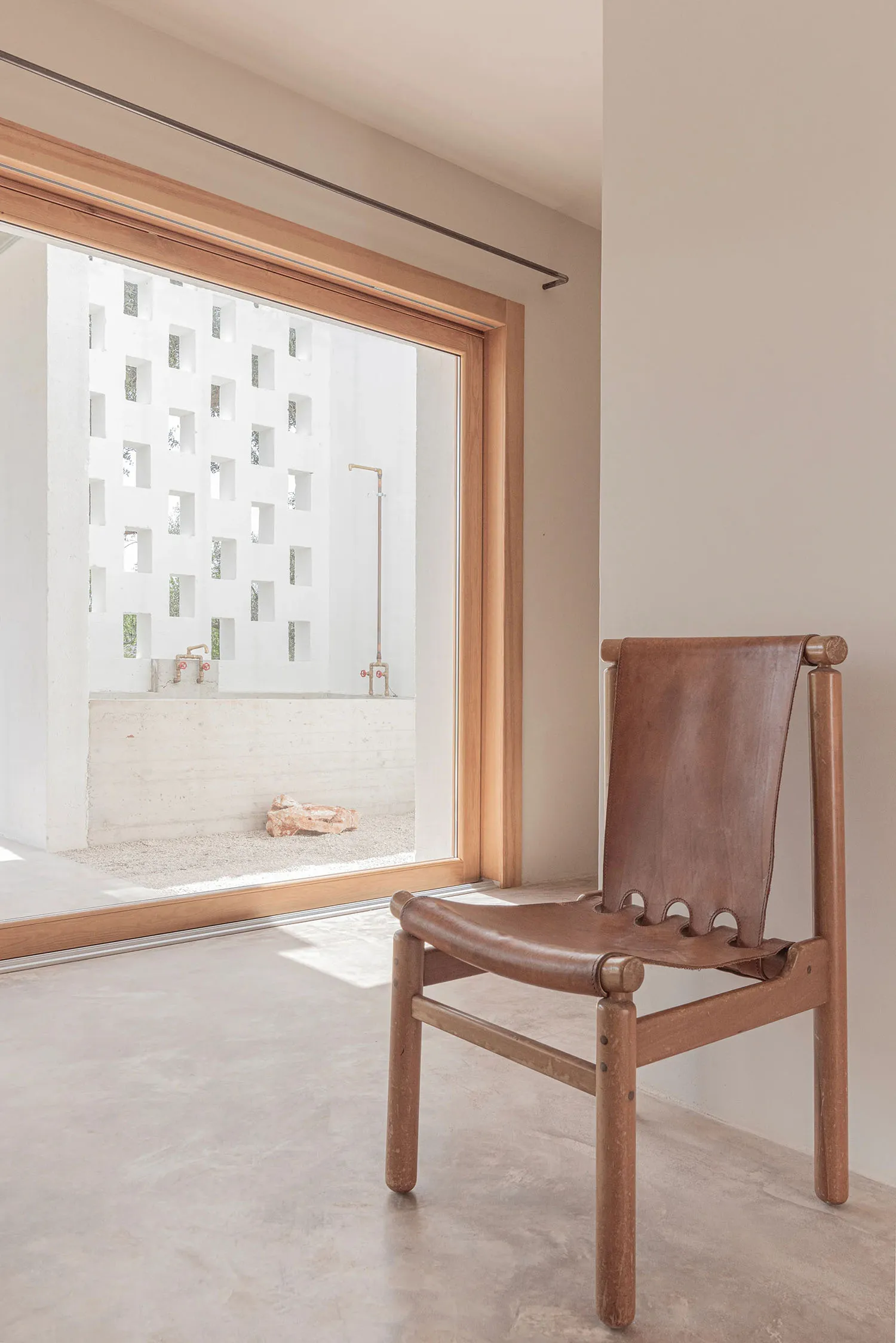 A minimalist interior with concrete walls, wooden floor, and a leather chair.