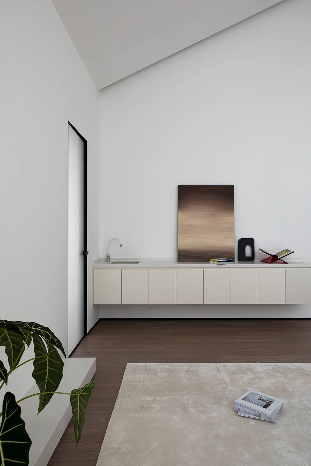 A minimalist living space featuring a wooden floor and a white cabinet with a sink and artwork.
