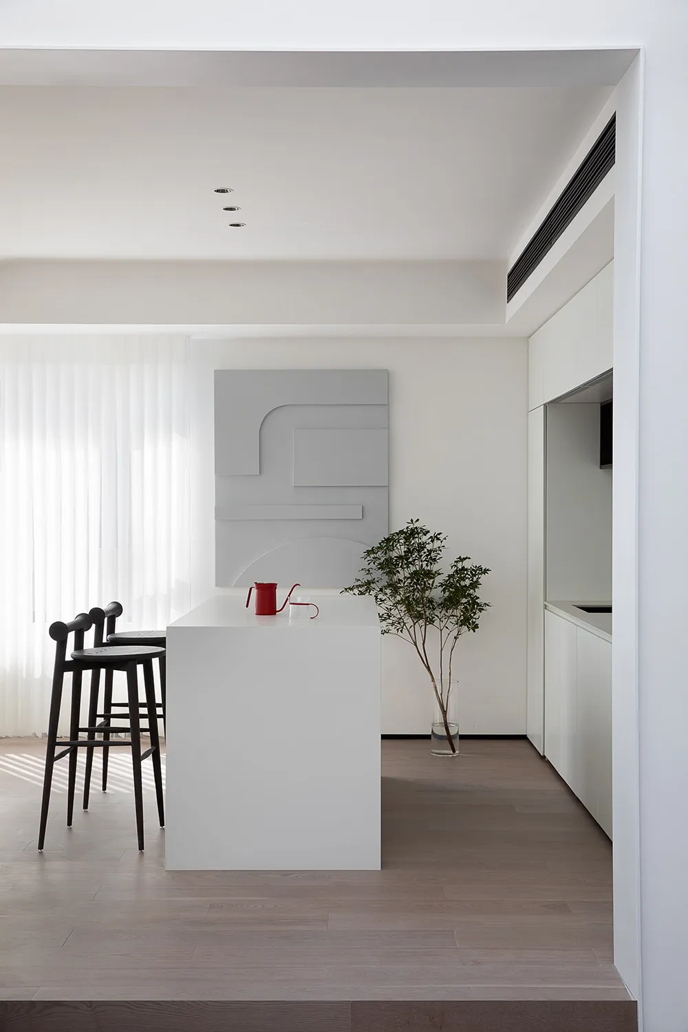 A minimalist residential kitchen with white surfaces and black stools.
