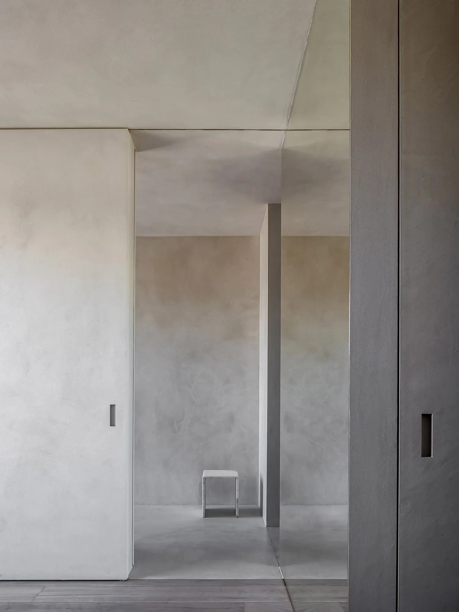 A minimalist concrete interior with a small white stool in a corridor.