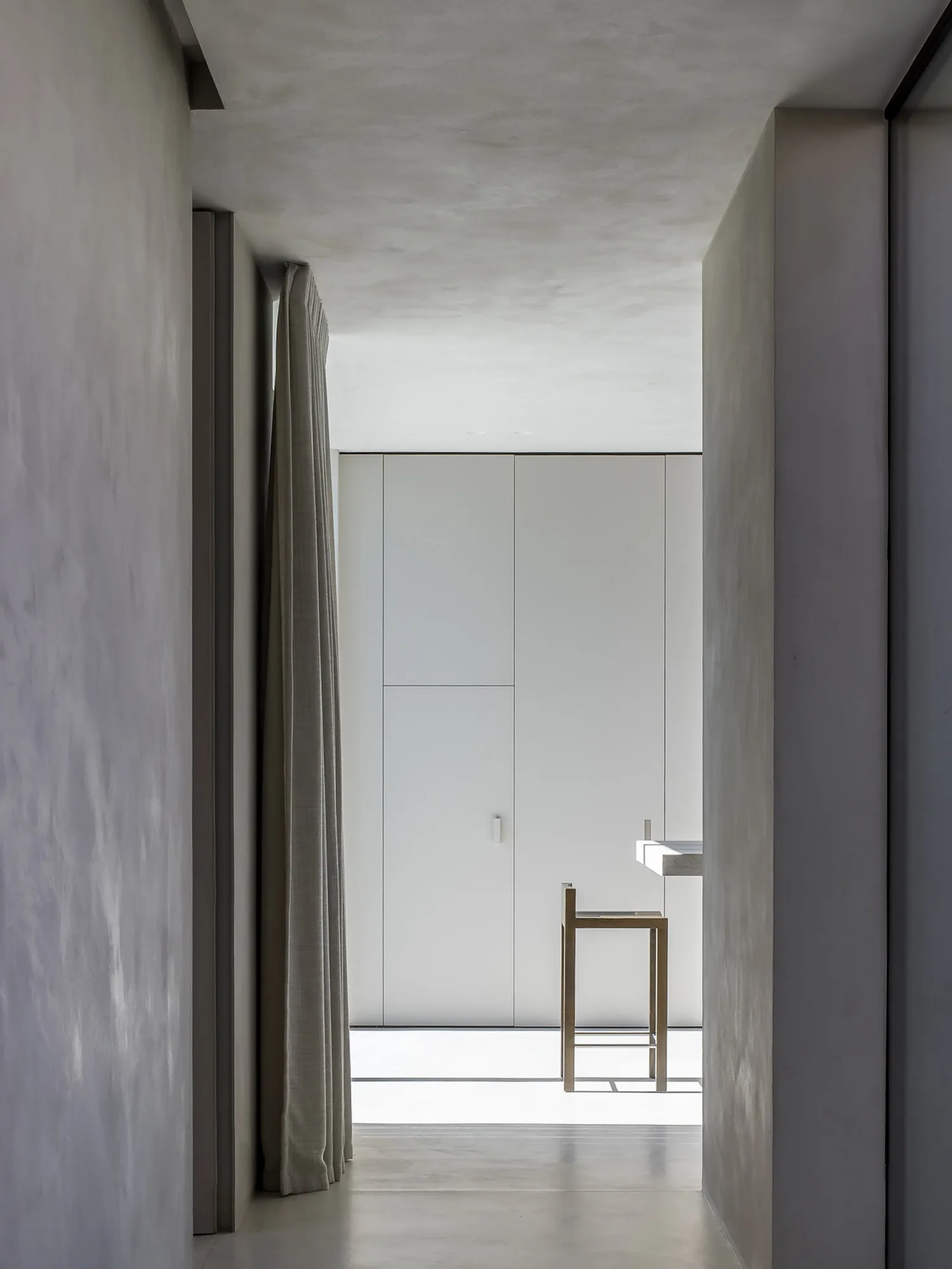 Minimalist white interior with concrete walls and floor, viewed through a narrow corridor.
