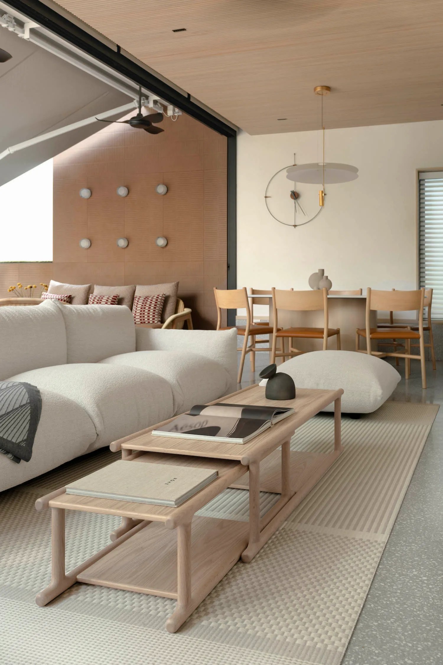 Minimalist living room featuring white and beige furniture, wood coffee tables, and a large beige rug.