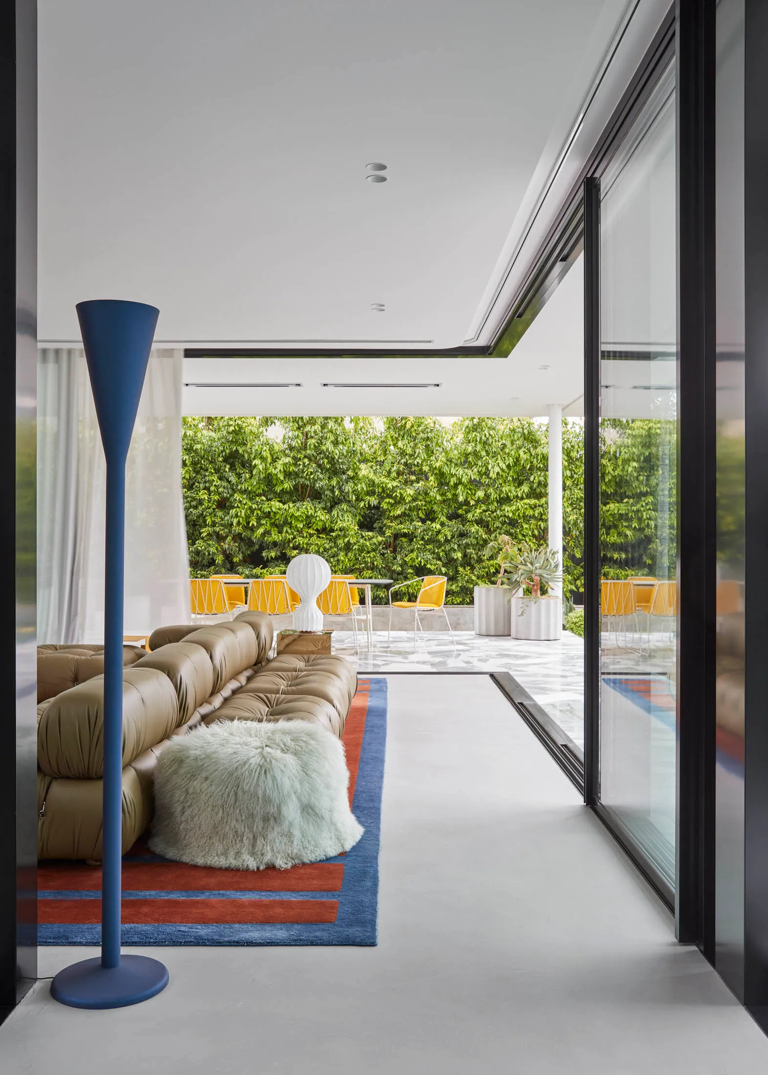 Modern living room with a concrete floor, glass sliding doors, and a green fur blanket.
