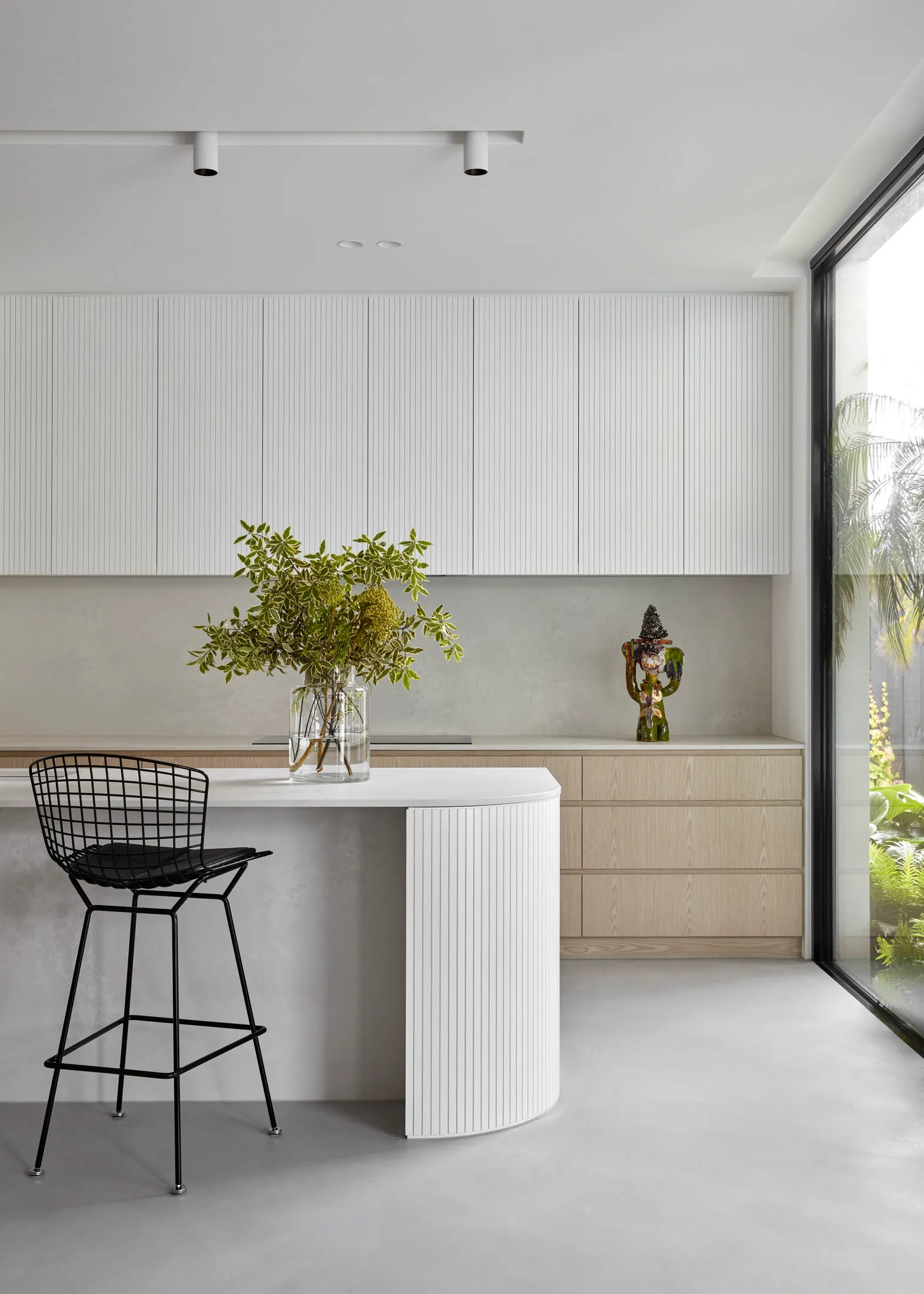 Modern minimalist kitchen with concrete countertops, white cabinets, and a black wire-frame barstool.