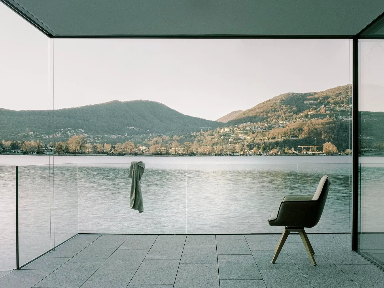 Modern residential interior with floor-to-ceiling glass walls overlooking a serene lake and mountains.