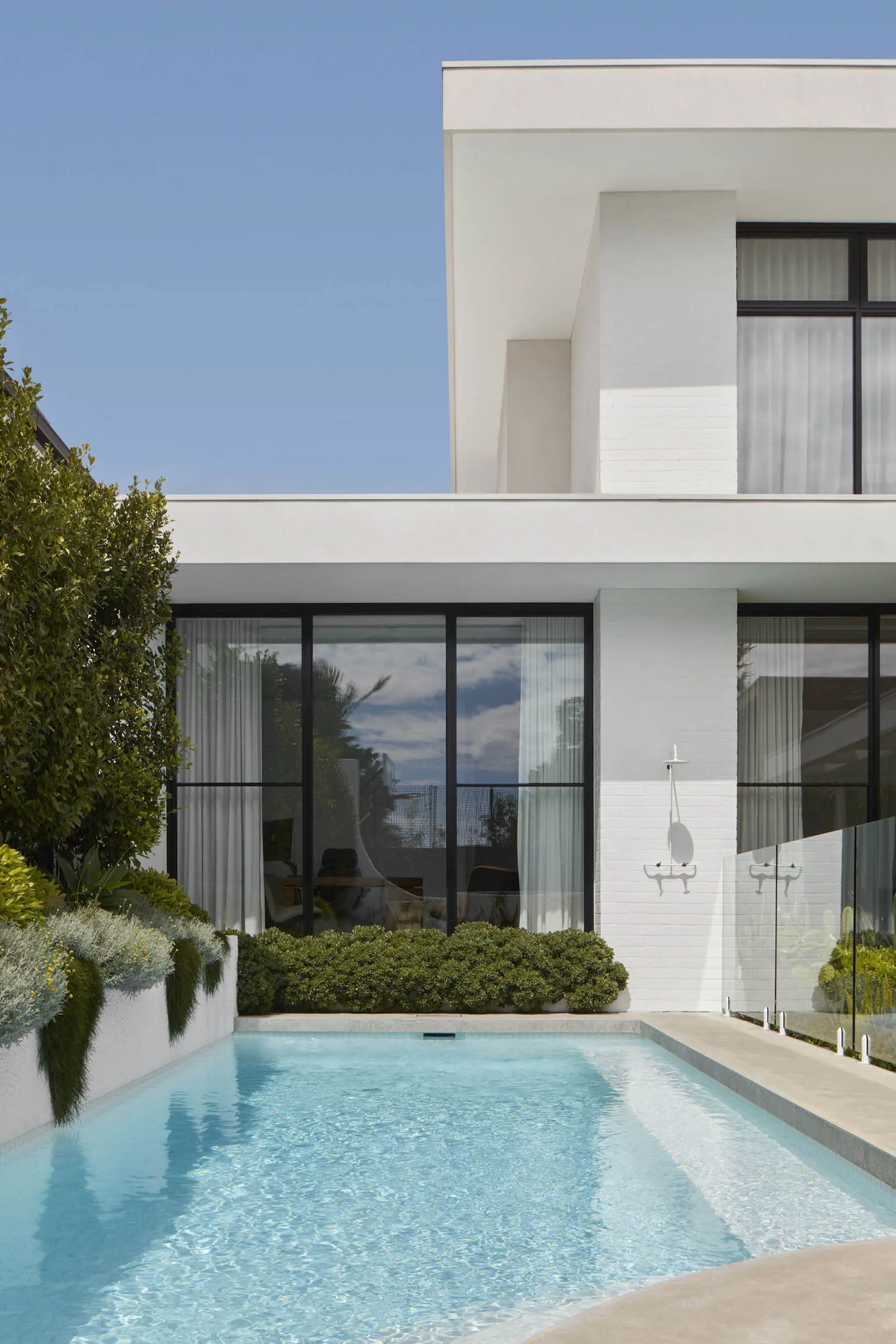 Modern minimalist two-story house with white stucco exterior and large glass windows.