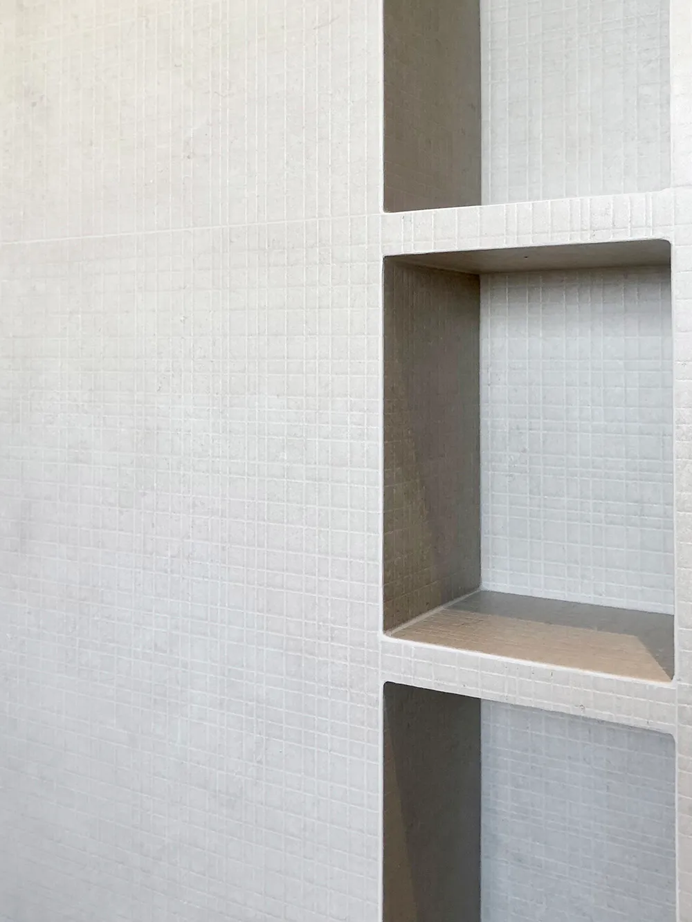 A minimalist design featuring a textured concrete wall with recessed shelves.