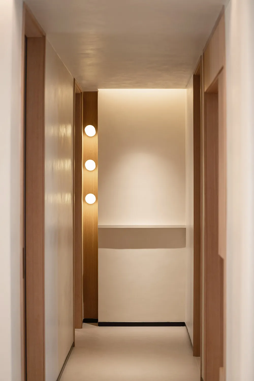 A minimalist corridor with wood panels and white painted walls, featuring round lighting fixtures.