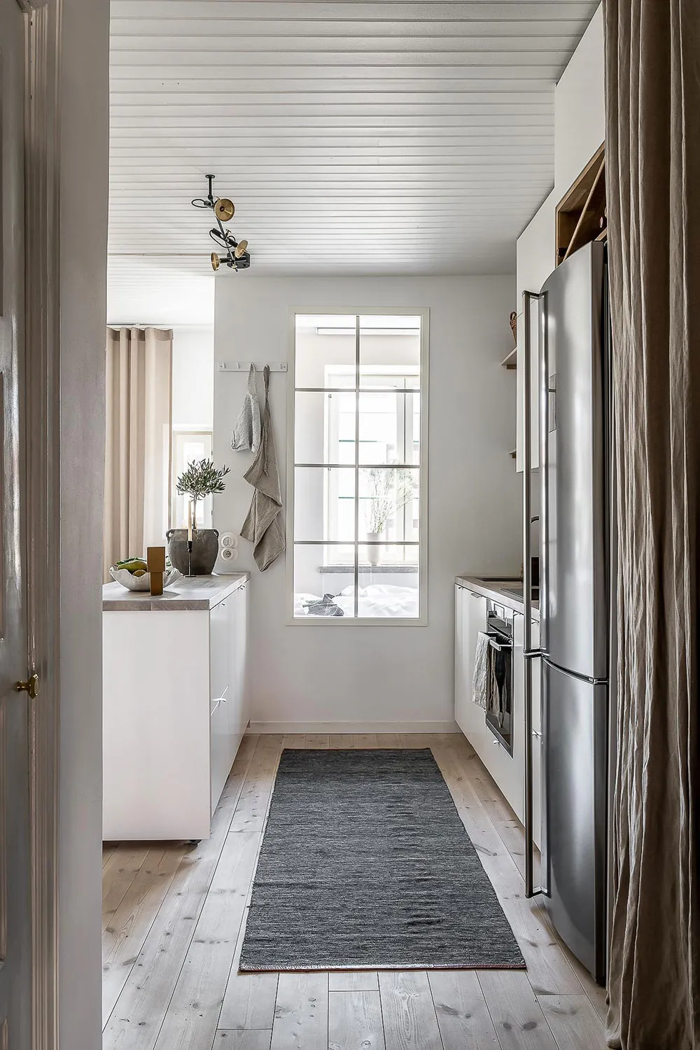 A minimalist kitchen with wooden flooring, featuring stainless steel appliances and a cozy, modern atmosphere.