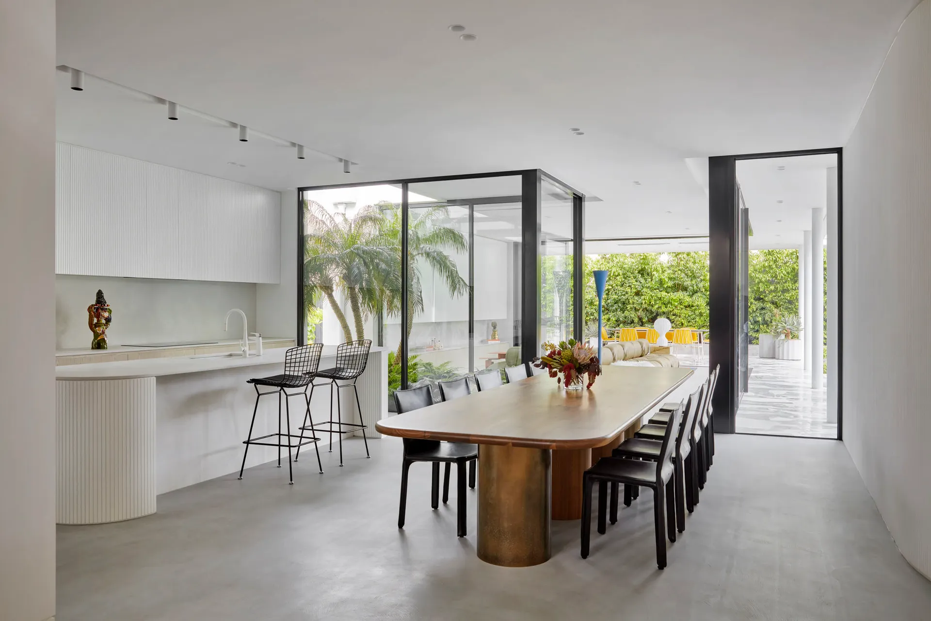 Modern dining room with transparent glass walls and a large wooden table surrounded by black chairs.
