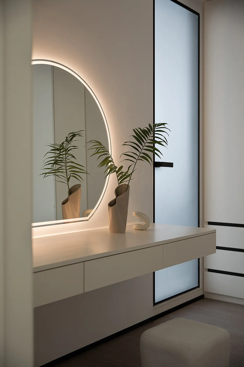 A modern white dresser with sleek, minimalist design features a large circular mirror with ambient lighting and a small potte