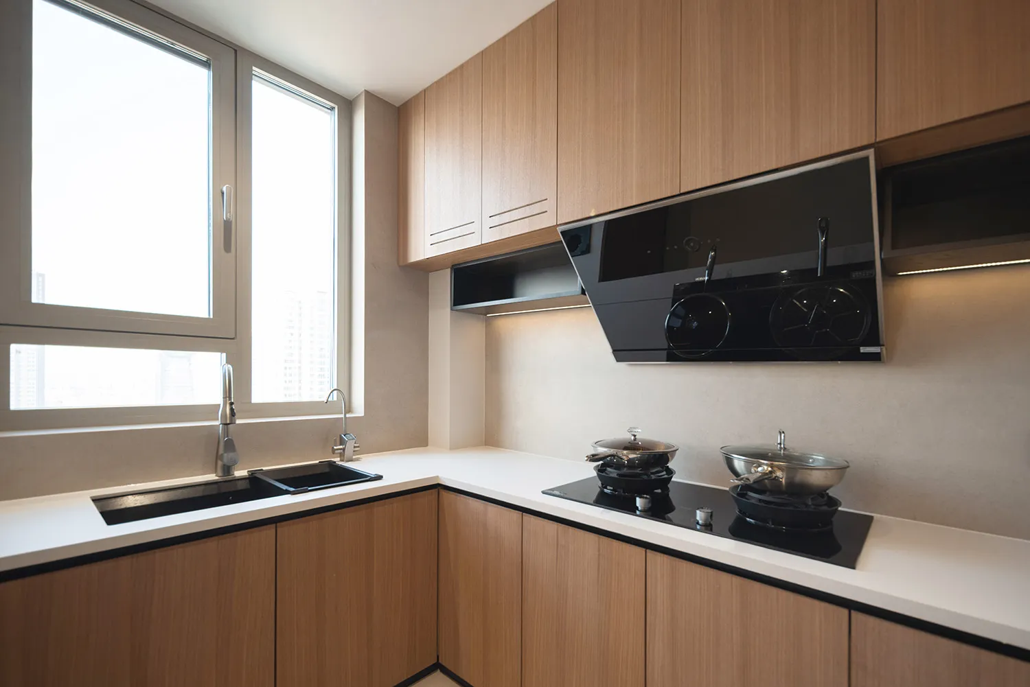 Modern minimalist kitchen featuring wood upper cabinets by a window, with a sleek countertop and black appliances.
