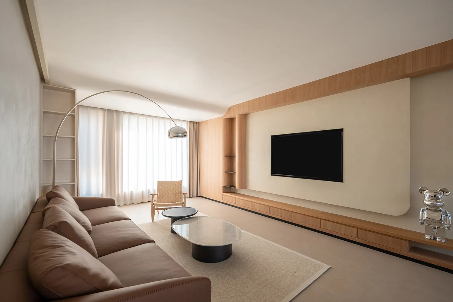 A modern minimalist living room with wooden furniture, a large window, and a television mounted on the wall.