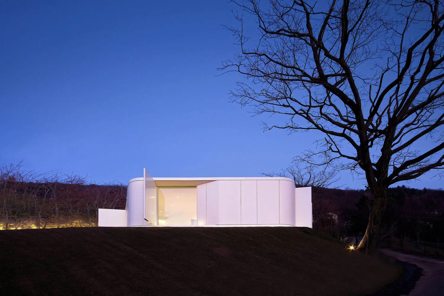 A minimalist residential exterior with concrete structure and large glass windows.