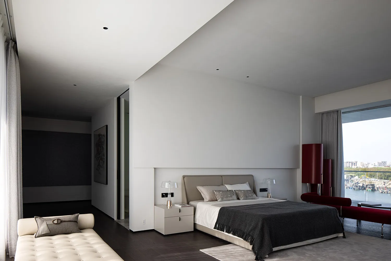A modern bedroom featuring taupe and gray tones, with a large bed, nightstands, and a couch by a window.