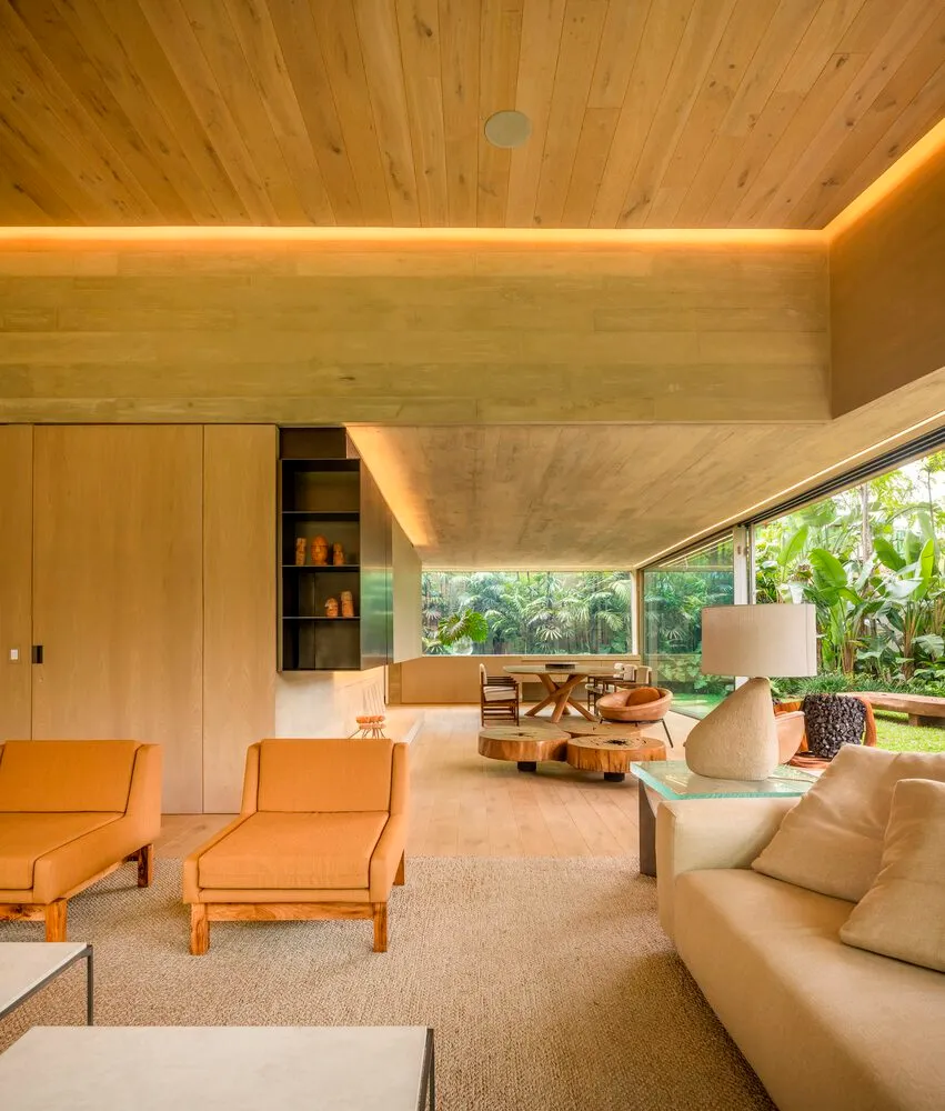 Modern living room interior with wooden floors, walls, and ceiling, featuring orange furniture and a glass coffee table.