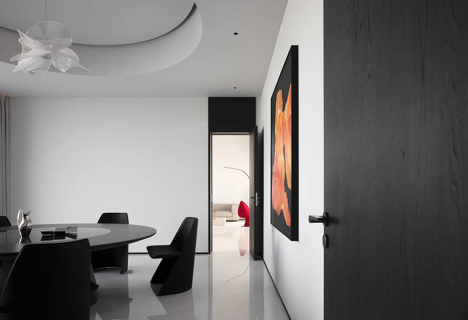 A modern dining room featuring a circular table with black chairs, located near a black door with decorative handles and an o
