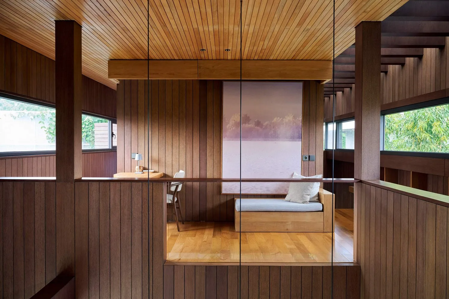 A minimalist living room with wooden walls, floor, and ceiling, featuring a small couch and a large window.