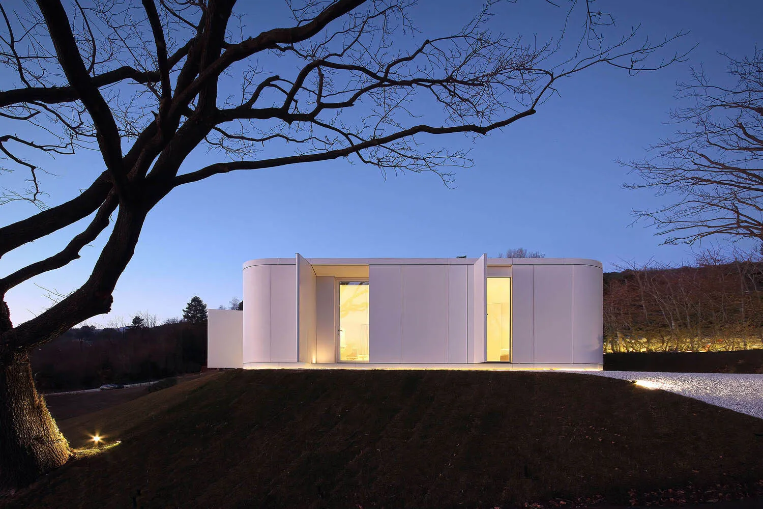 A modern house with white curved panels illuminated at dusk.