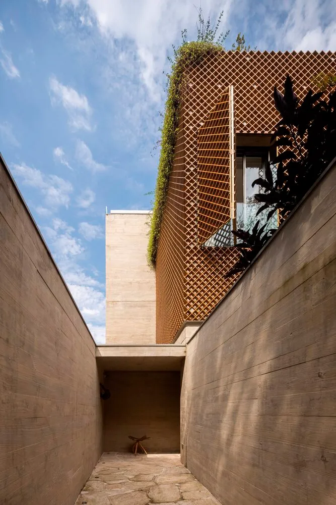 Modern exterior of a building with wooden deck and green plants on the roof, against a blue sky with white clouds.