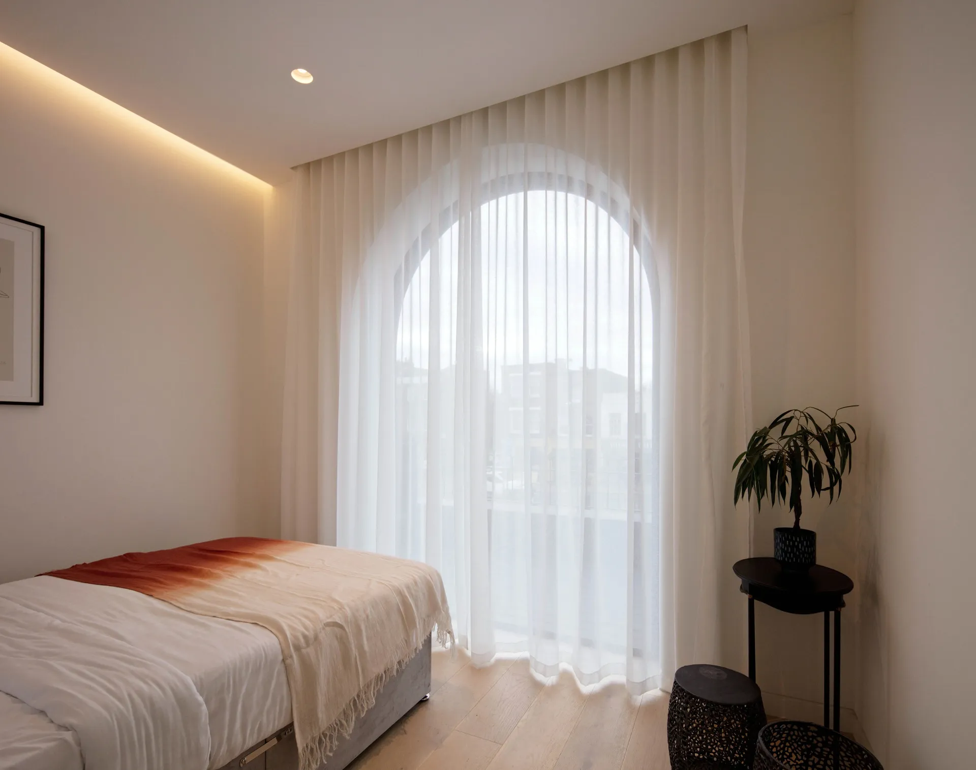 Modern minimalist bedroom featuring a bed with white bedding and sheer white curtains, minimalistic decor, and a small round