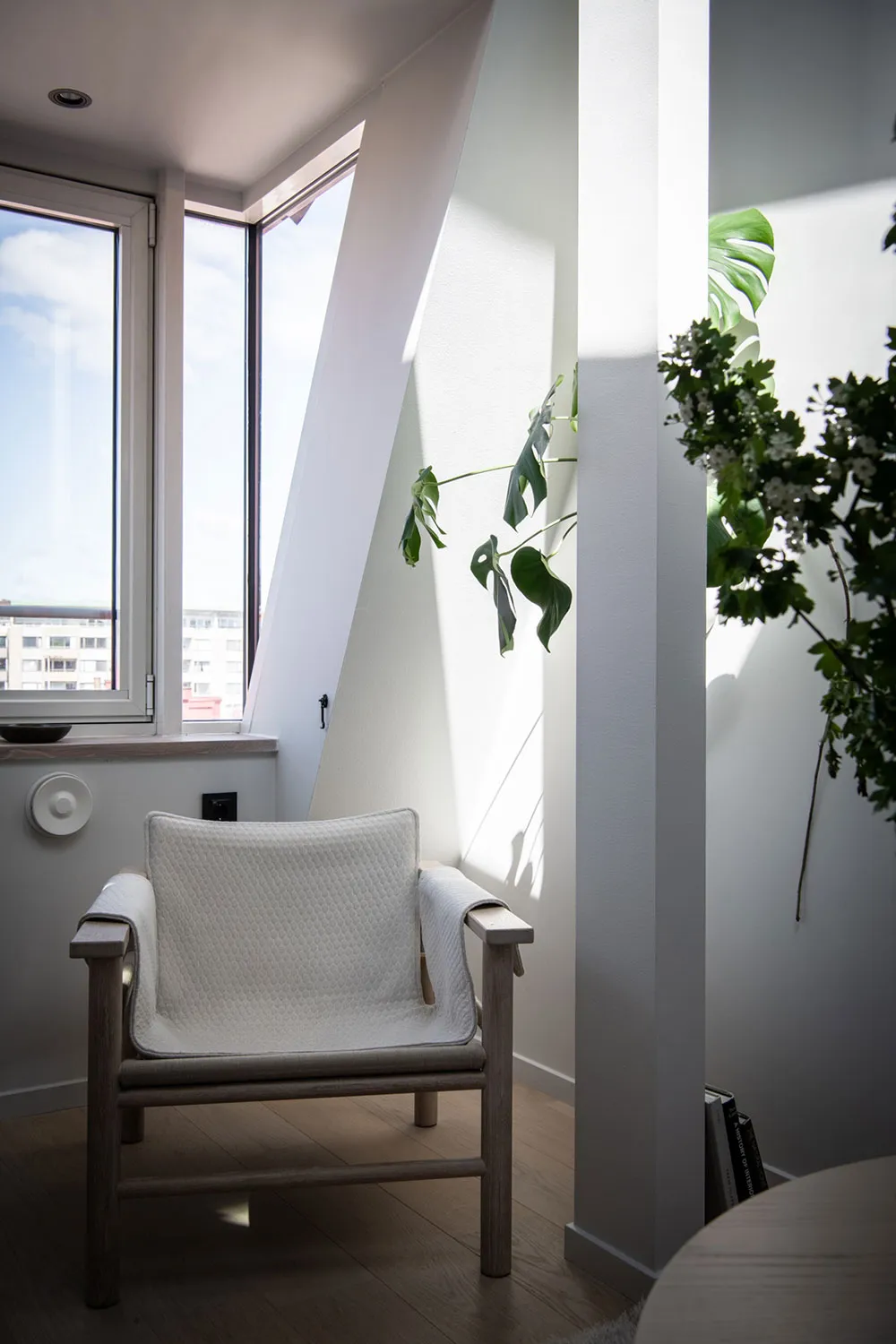 A modern interior featuring a white upholstered chair with wooden arms and legs, positioned near a window.