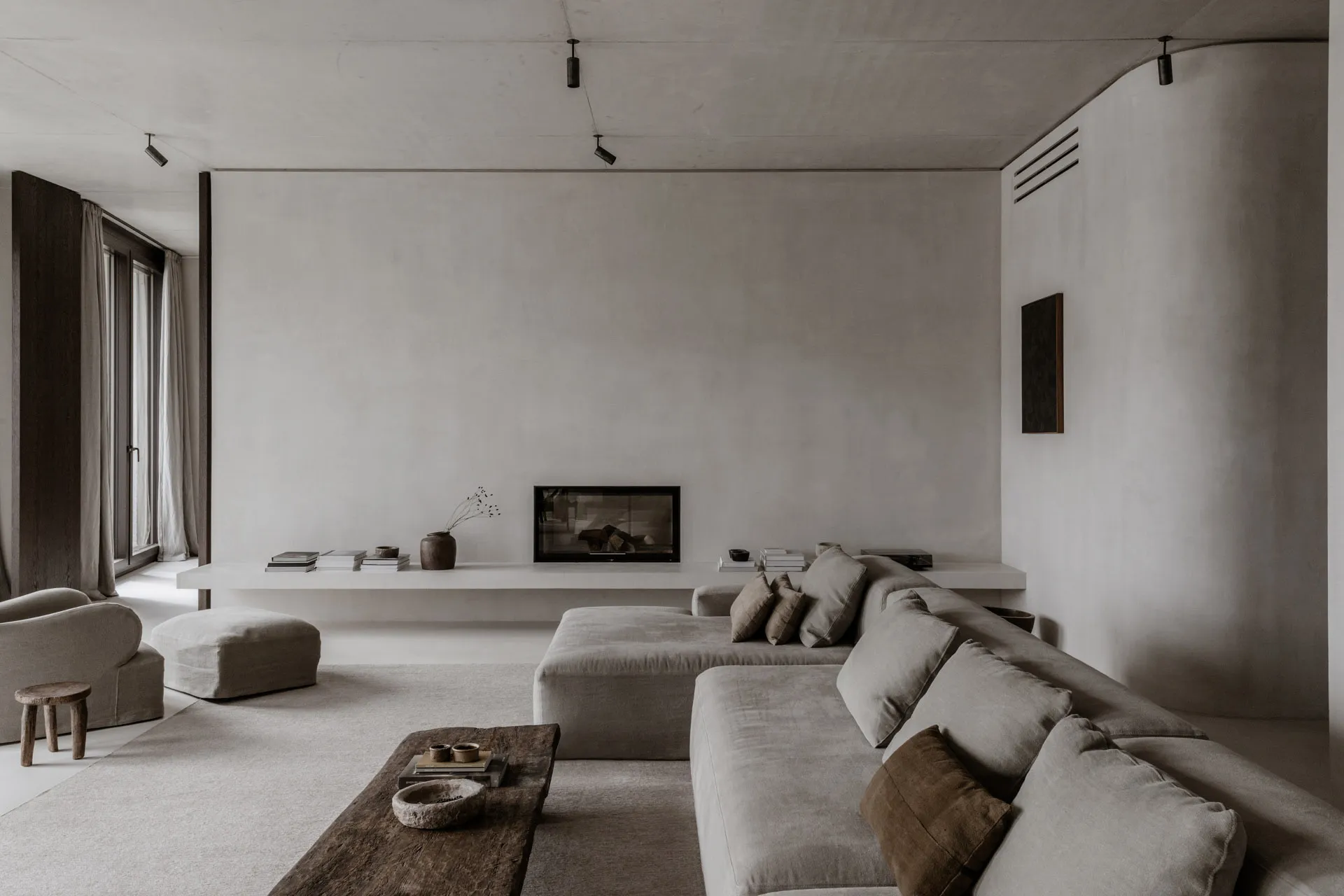 A minimalist living room featuring concrete walls, a large sectional sofa, and a low-profile coffee table.