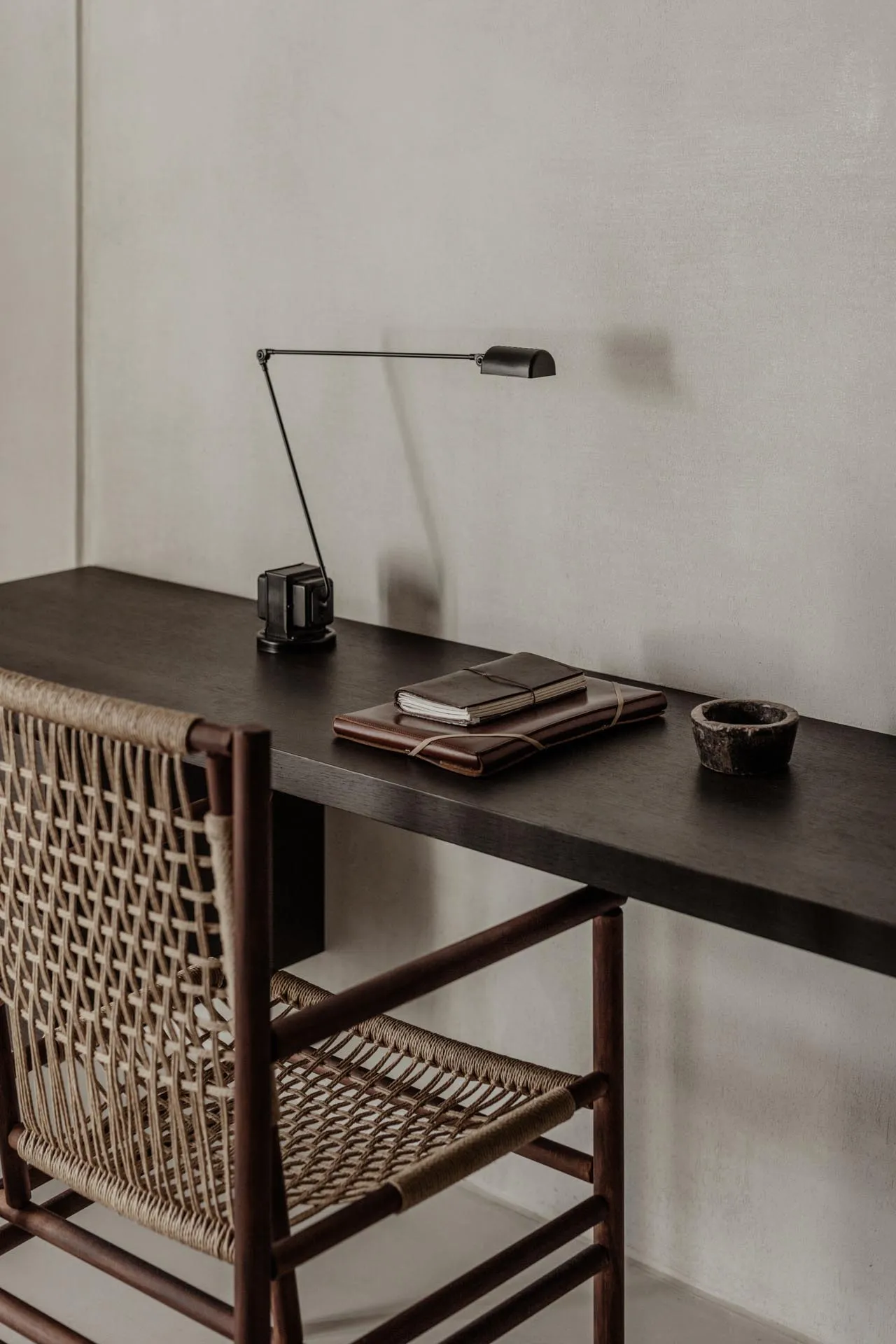 A modern desk setup with a wooden desk, a woven leather chair, and a metal desk lamp.