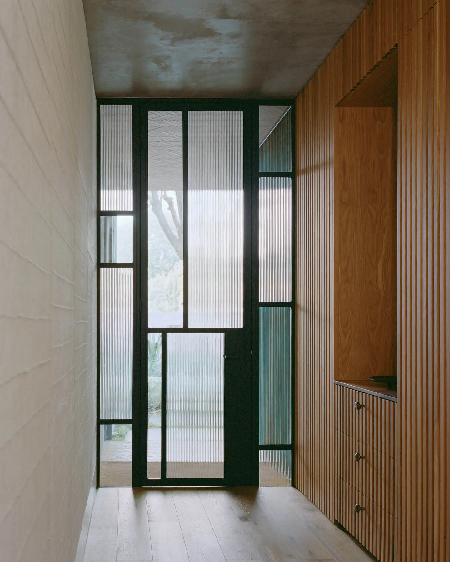 Modern minimalist entryway with glass panels and wooden detailing.