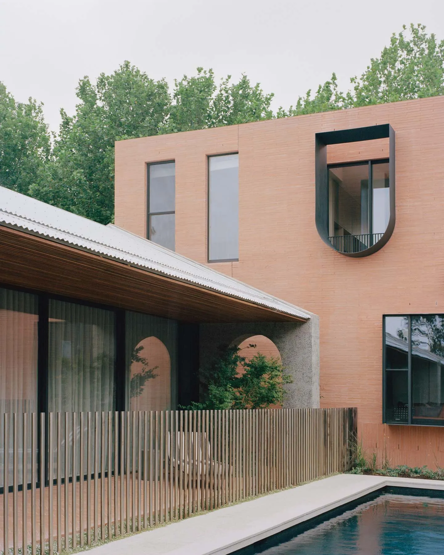 Modern house exterior featuring clay brick, concrete walls and large windows.