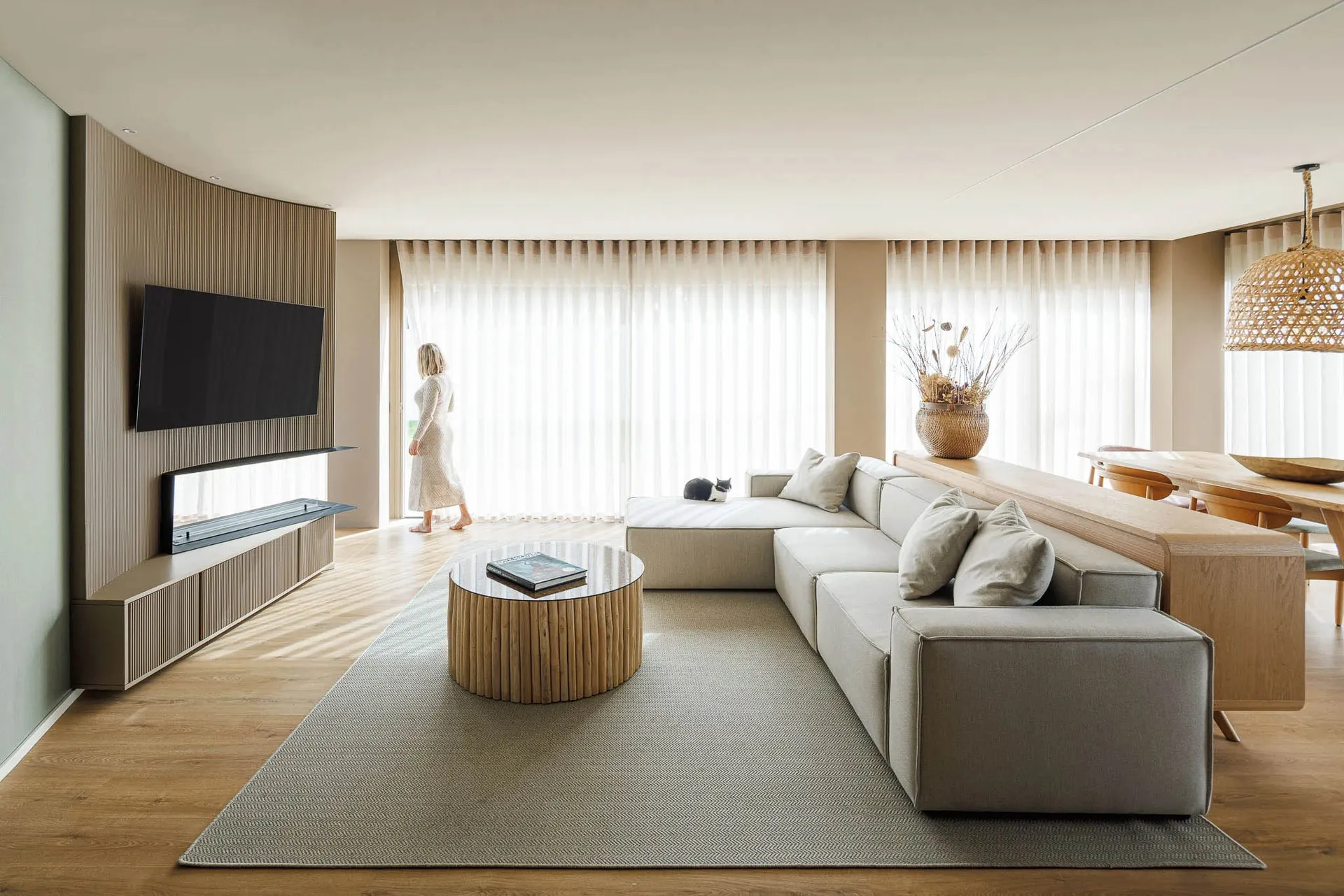 A modern, minimalist living room featuring a sectional sofa, round wooden coffee table, and a wall-mounted television.