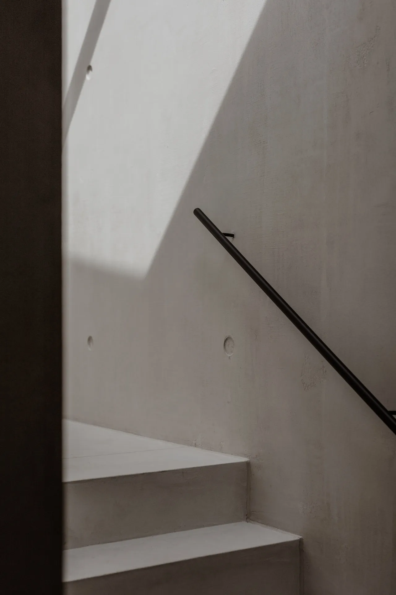 A minimalist staircase with a concrete wall and a black handrail.