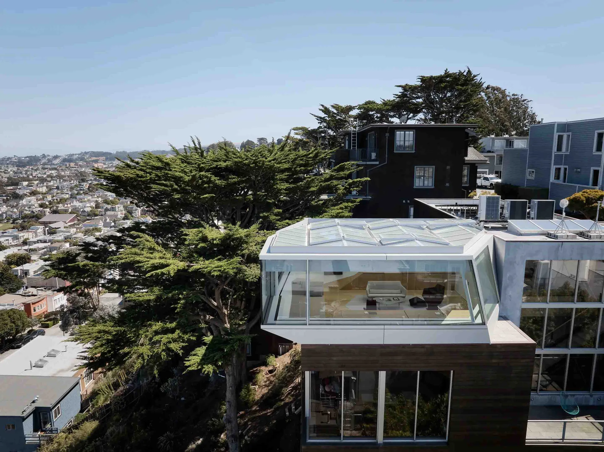 A modern residential building with glass walls and wooden elements, featuring a glass roof and a living room with a couch.